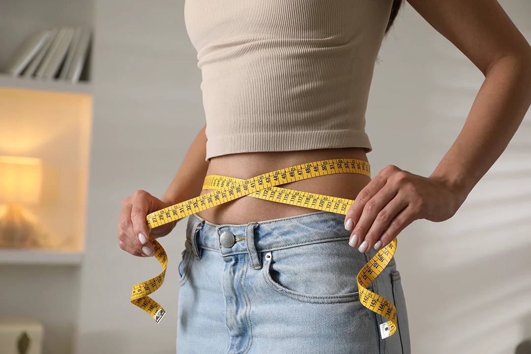 A close-up of a woman measuring her waist with a yellow tape measure, highlighting semaglutide in Houston for weight management.