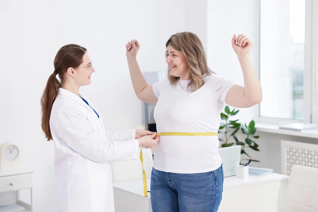 Excited patient celebrates progress as doctor checks waist measurement at weight loss clinic Houston in bright office.
