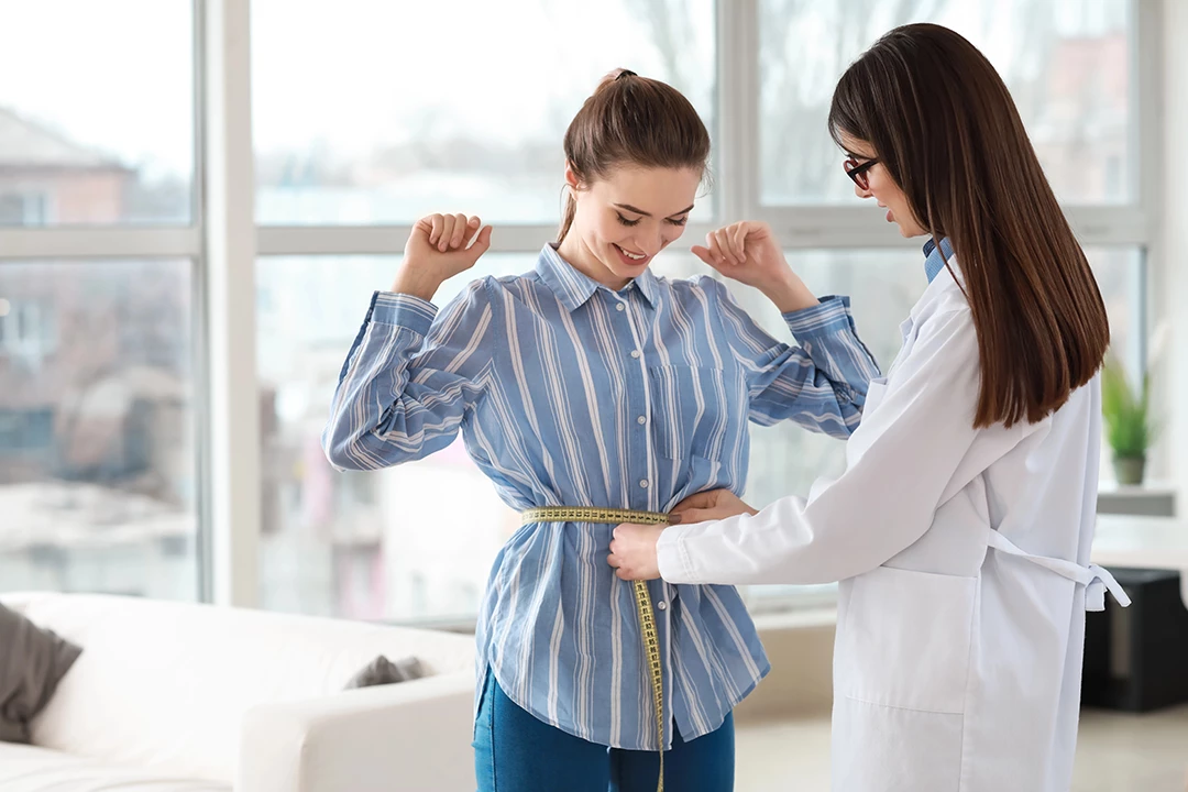 Smiling patient gets waist measured by doctor discussing semaglutide cost Houston in a sunny medical consultation room.