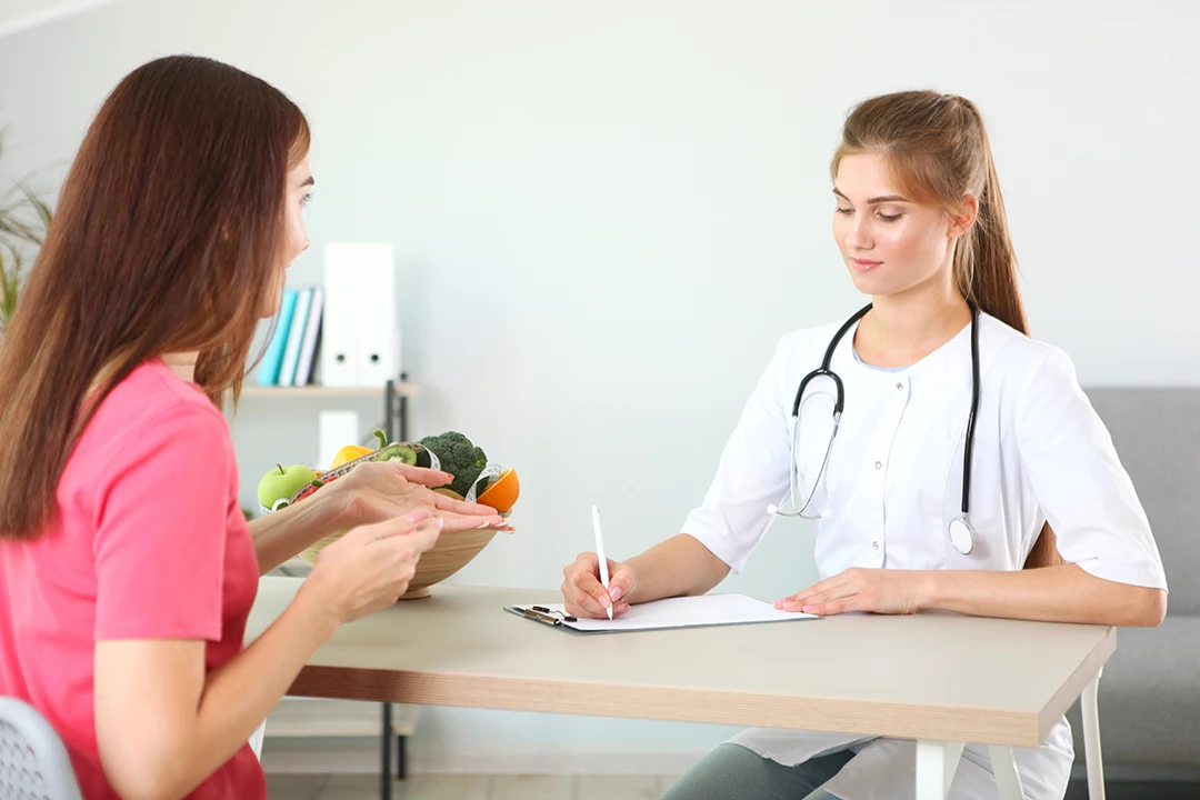 Patient discusses healthy eating with doctor holding fruit bowl at weight loss clinic Houston in a relaxed consultation.