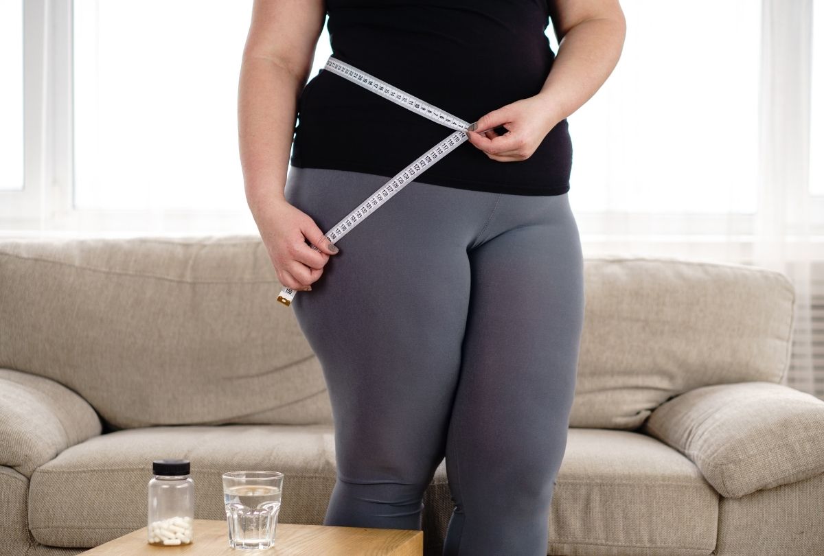 Woman tracking waist size at home with pills and water, highlighting Weight Loss Injections Houston benefits