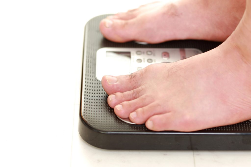 Close-up of feet on digital scale tracking weight loss progress under care of experienced weight loss doctor in Houston, essential for monitoring health and fitness goals.