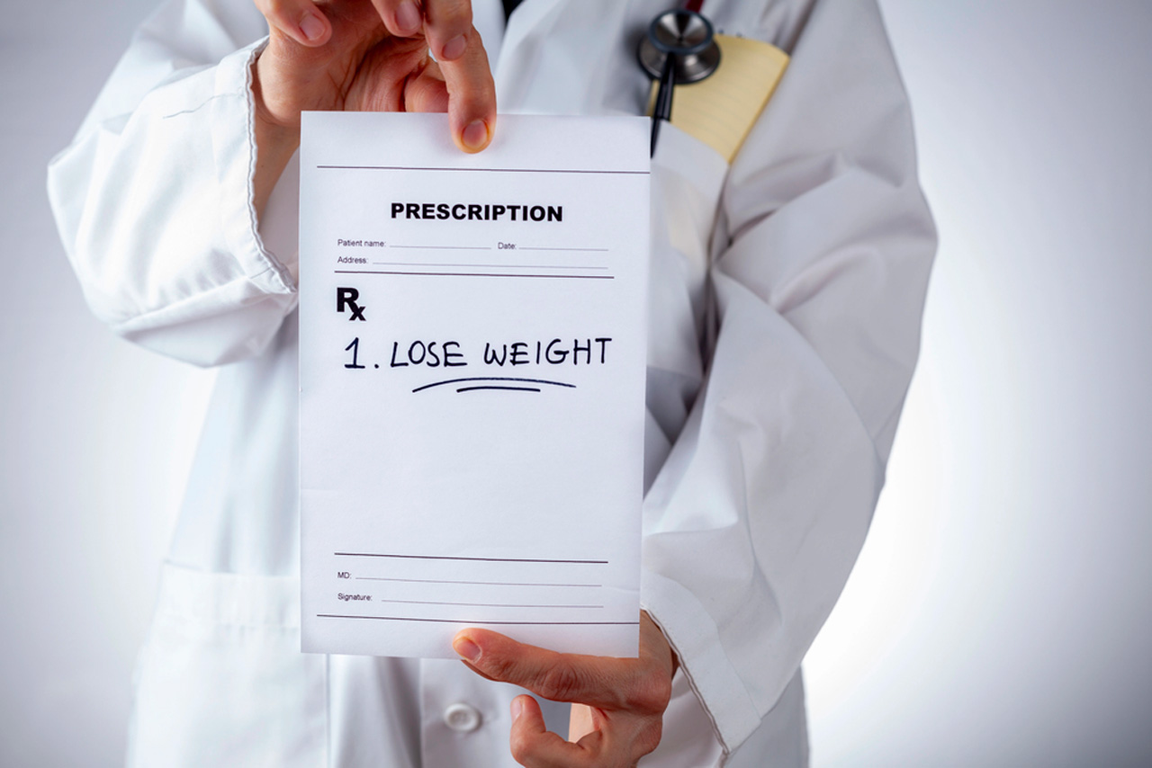 Doctor in white coat holding prescription pad with 'Lose Weight' instruction, provided by expert weight loss doctor in Houston for personalized health plans.