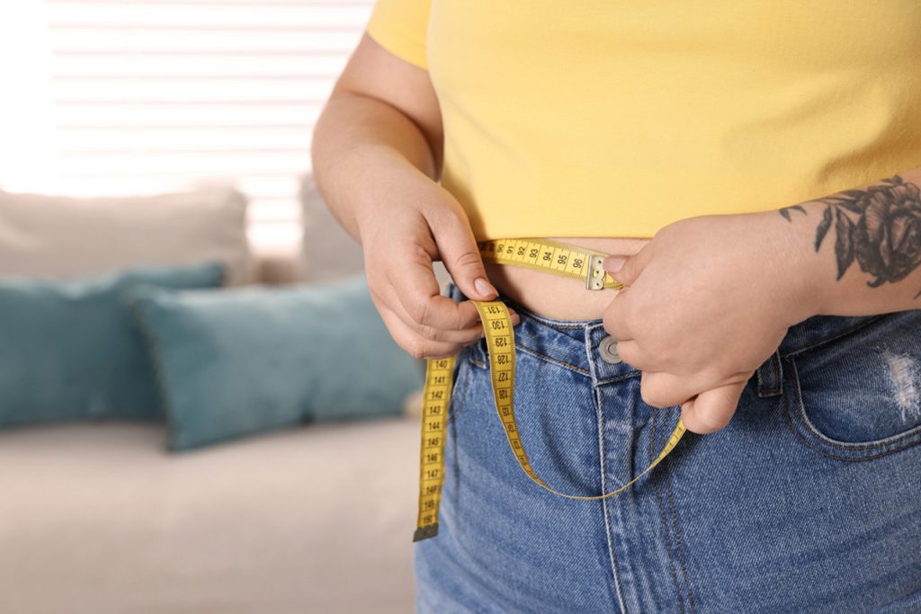 Person measuring waist with tape at home, representing progress and body changes from personalized Medical Weight Loss Houston programs.