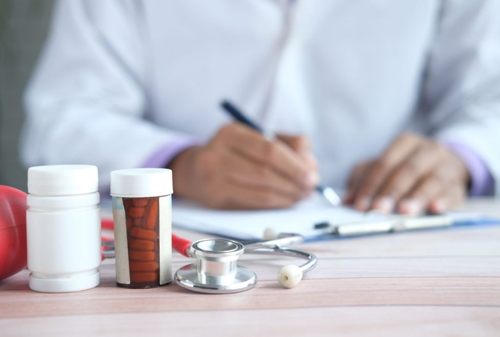 Healthcare provider in white coat writing on clipboard beside pill bottles and stethoscope, representing prescription decisions in weight loss care.