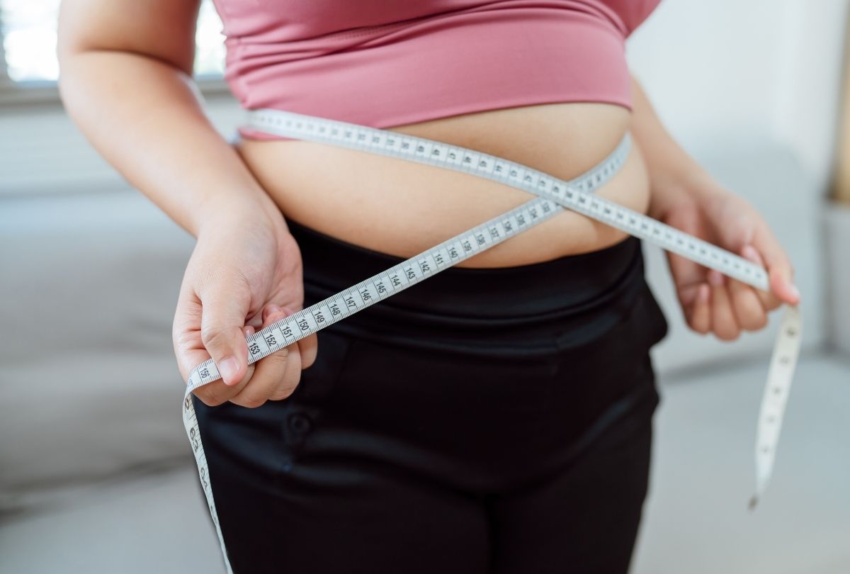 Woman measuring waist with tape, tracking inches for weight loss at semaglutide Houston clinic, pink top and black pants.