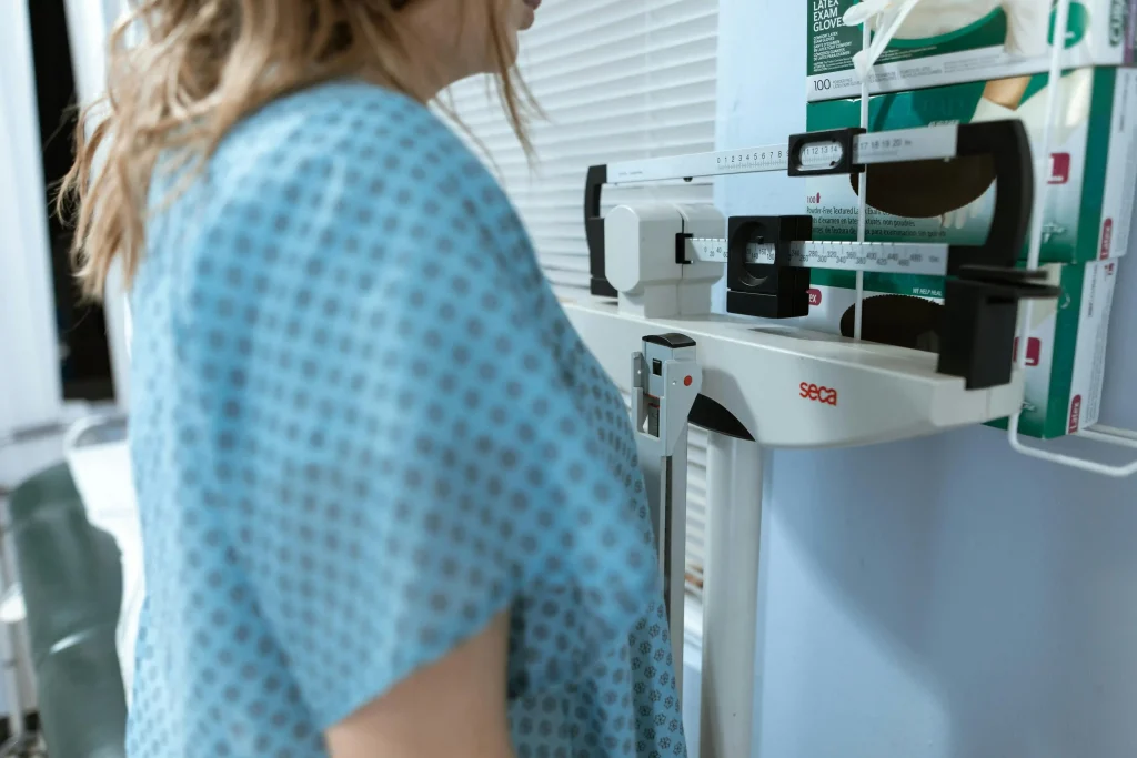 A patient in a medical gown stands on a professional scale at the NewShape Weight Loss Clinic program facility.