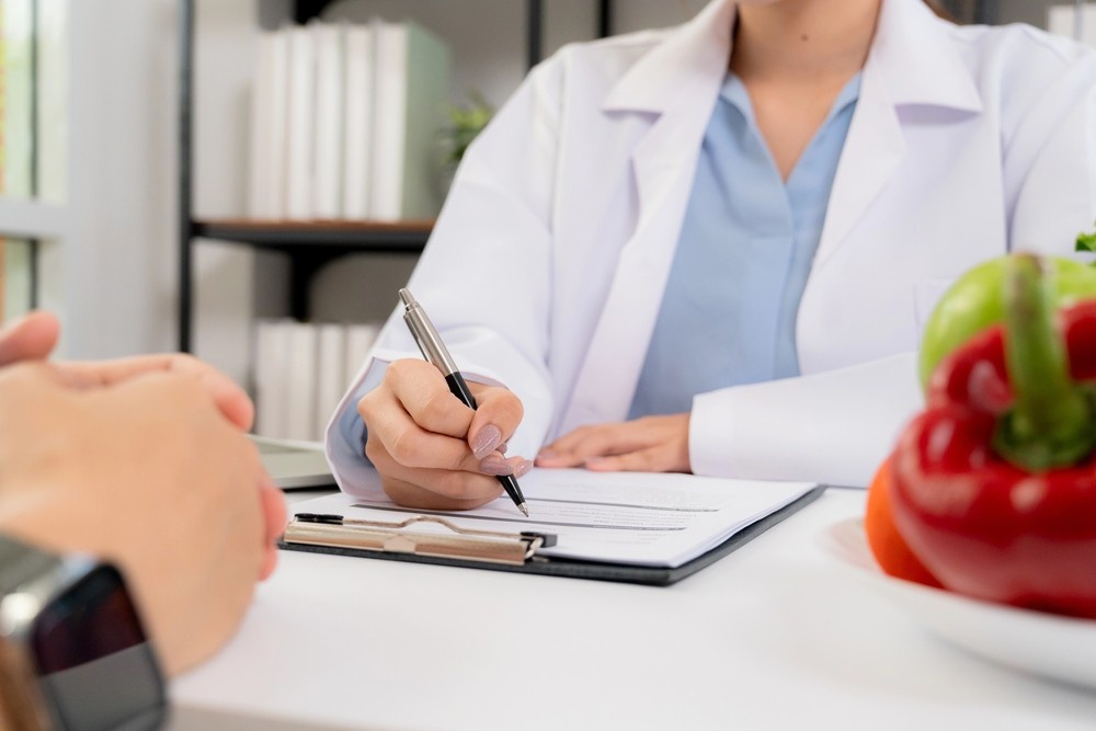 A weight loss doctor Houston consulting with a patient and writing notes on a clipboard during a clinic visit.