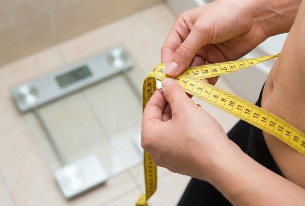 Woman measuring her waist with a tape measure to track results from GLP-1 weight loss Houston program