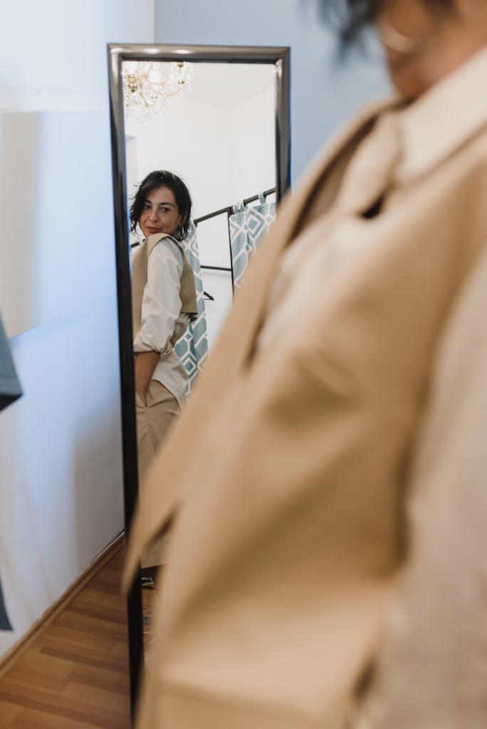 Woman trying on a beige outfit, gazing at her reflection in the mirror indoors.