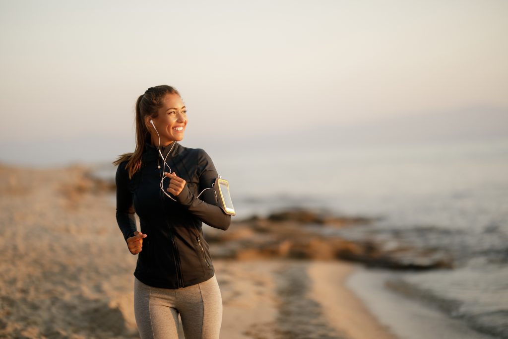 Young happy athletic woman feeling motivated while running at the beach. Copy space.