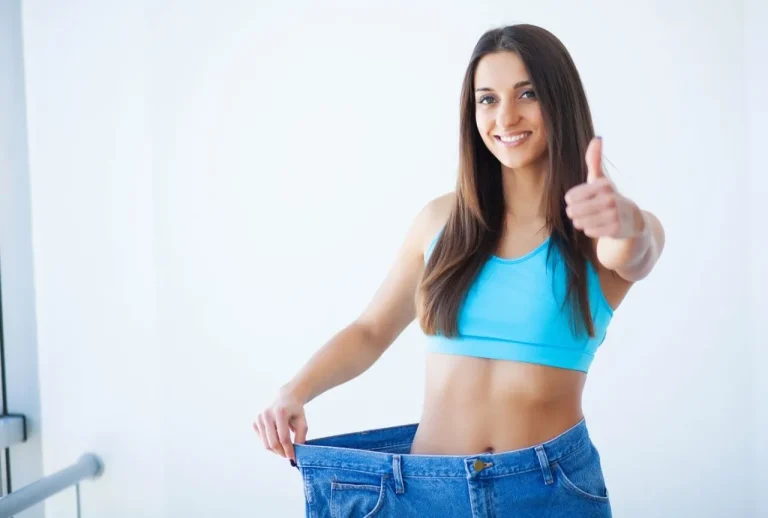 Fit woman in oversized jeans celebrating weight loss success from tirzepatide treatment available in Houston.