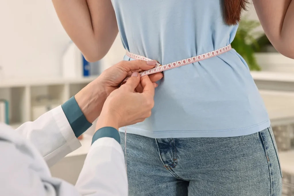 Medical professional measures patient's waist size, monitoring successful weight loss with tirzepatide in Houston.