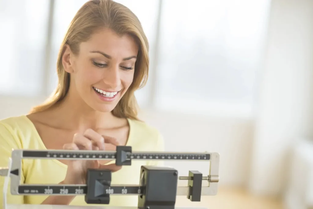 A smiling woman weighs herself on a medical scale in Houston, celebrating progress with tirzepatide treatment.