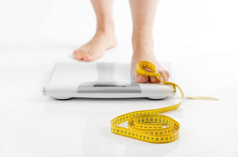 A person stands on a scale with a measuring tape, tracking progress after getting weight loss shots Houston.