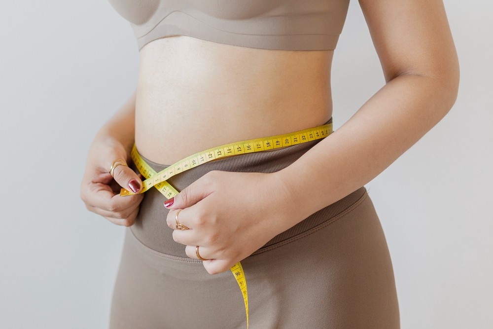 A woman in athletic wear measures her waistline with a tape measure after starting weight loss shots Houston.